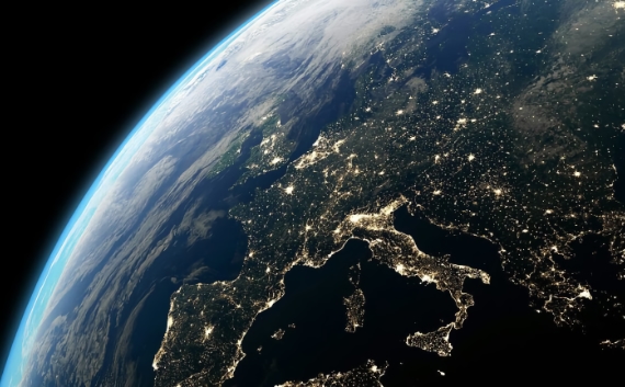 Night-time view of Earth from space showing Europe illuminated by city lights, with Italy's distinctive boot shape clearly visible against the dark Mediterranean Sea